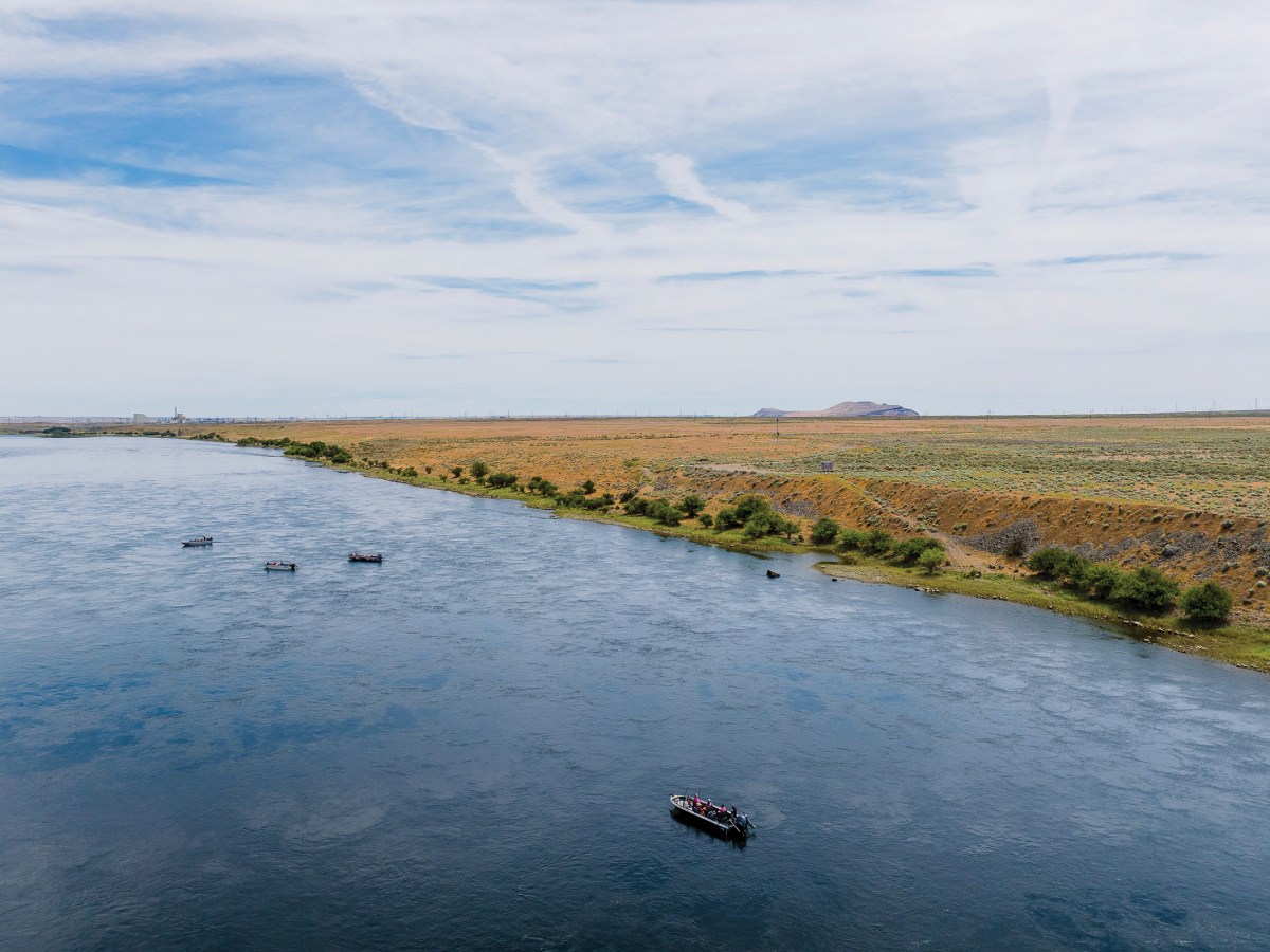 Boats carry Hanford Journey attendees down the Columbia River in Washington toward Hanford reactors, one that’s cocooned and another that’s decommissioned but still standing.