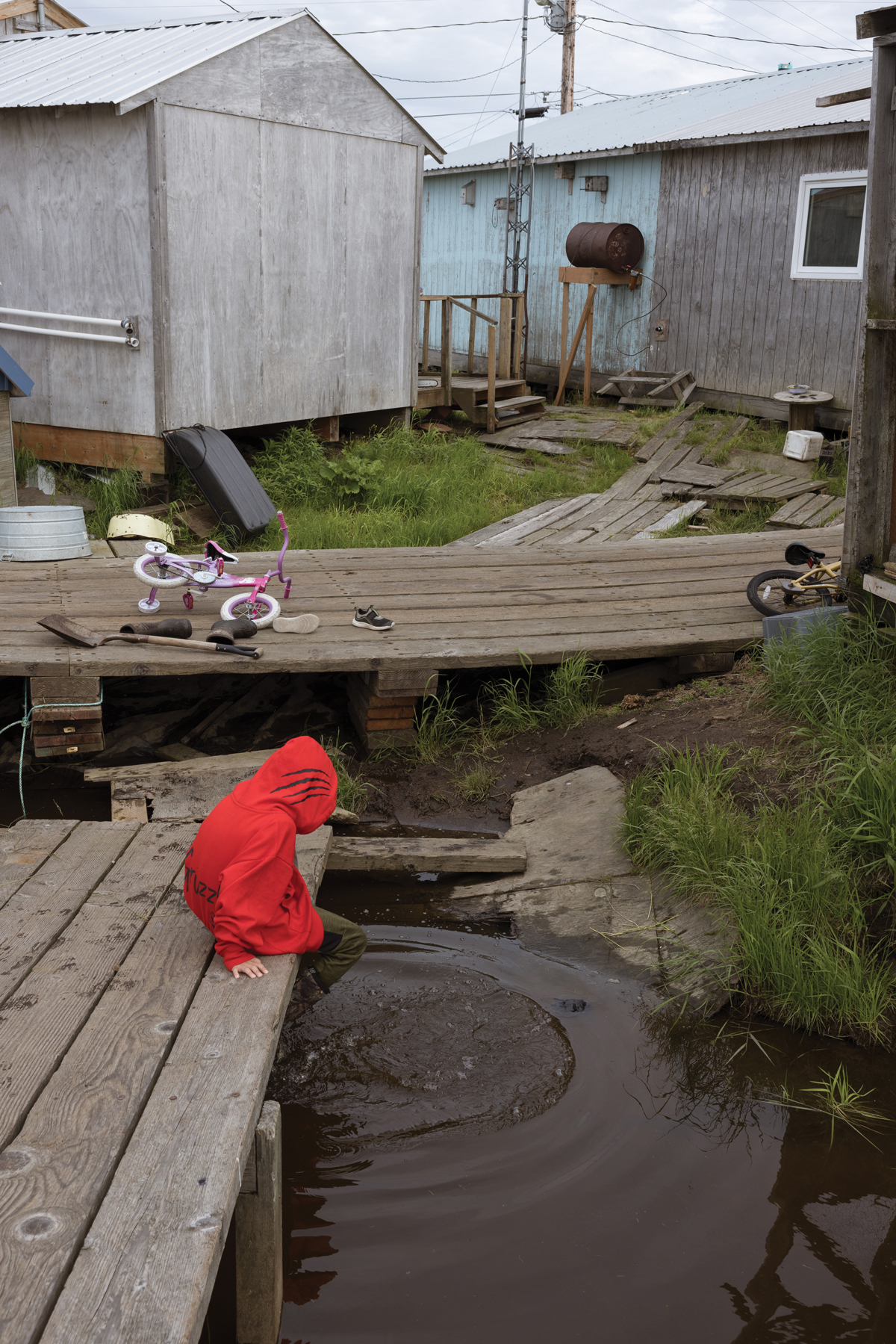 Kenton Isaac, 5, one of Susanna Isaac’s grandchildren, splashes his feet in the water near his home in Akiuk, the older side of Kasigluk. “Come spring, the water goes all the way under the sidewalks we walk on,” Susanna Isaac said this summer. The spring floodwaters still had not receded by mid-July.